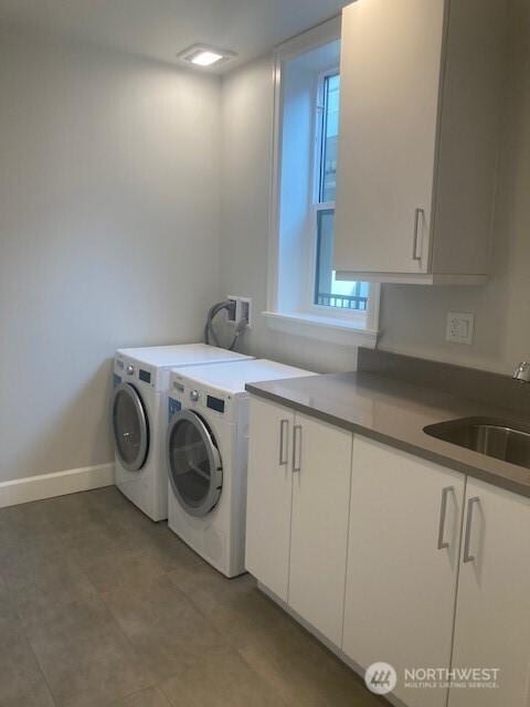 clothes washing area with independent washer and dryer, a sink, cabinet space, and baseboards