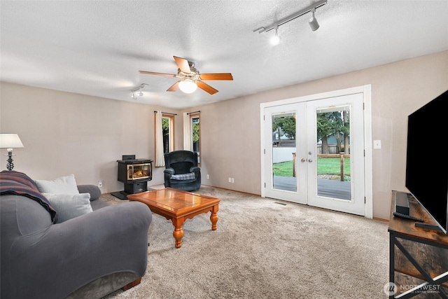 carpeted living room with french doors, baseboards, a textured ceiling, and a wood stove