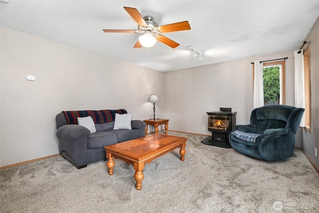 living room with a wood stove, carpet, baseboards, and ceiling fan