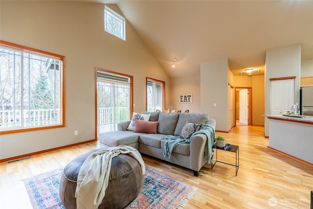 living area with high vaulted ceiling, visible vents, light wood-style flooring, and baseboards