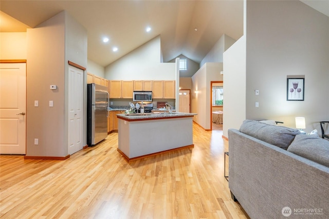 kitchen featuring appliances with stainless steel finishes, light wood-style floors, open floor plan, light brown cabinets, and high vaulted ceiling