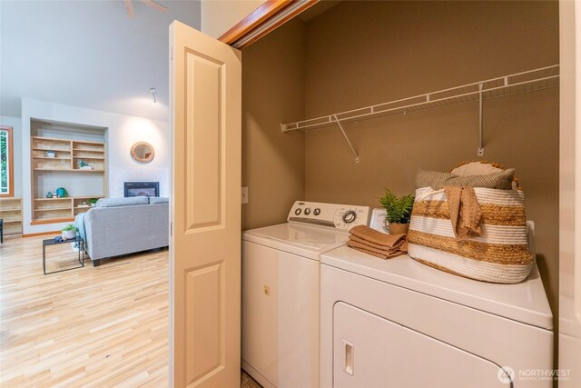 clothes washing area with built in features, light wood-style floors, a glass covered fireplace, washer and dryer, and laundry area