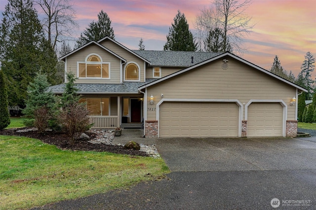 traditional-style home featuring roof with shingles, covered porch, a lawn, a garage, and driveway