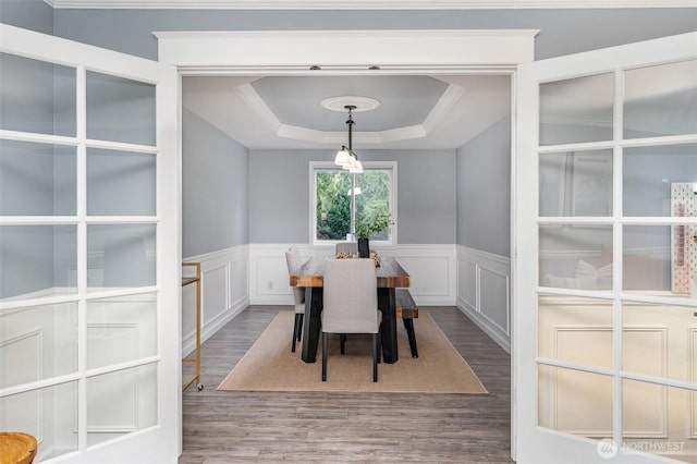 dining space with a wainscoted wall, a tray ceiling, and wood finished floors