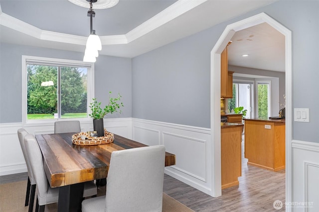 dining area with a wainscoted wall, a raised ceiling, and light wood-style flooring