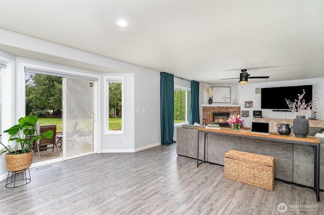 living room with baseboards, visible vents, a ceiling fan, wood finished floors, and a fireplace