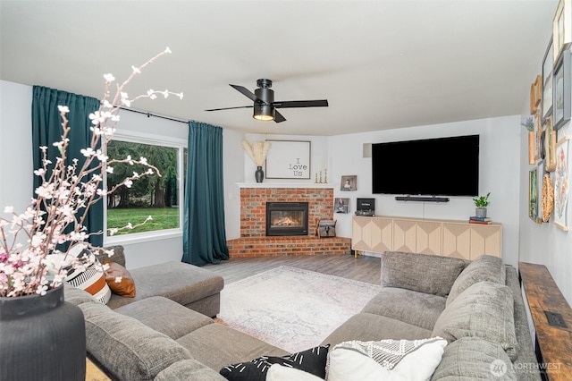 living area with a brick fireplace, ceiling fan, and wood finished floors