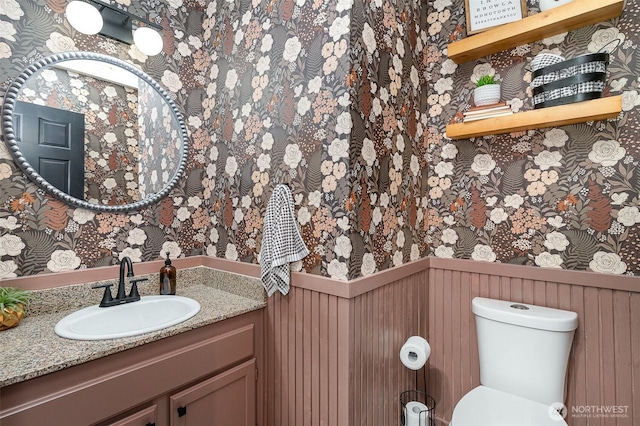 bathroom with a wainscoted wall, vanity, toilet, and wallpapered walls