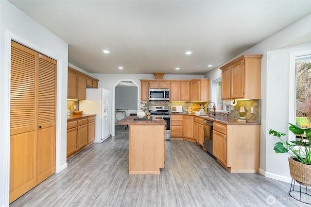 kitchen with arched walkways, decorative backsplash, light wood-style flooring, a center island, and stainless steel appliances