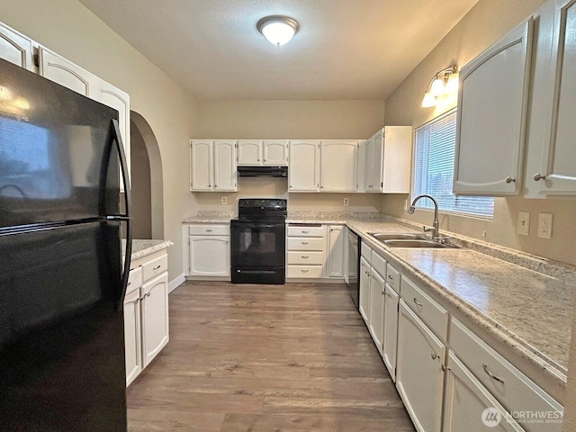 kitchen with white cabinets, under cabinet range hood, light countertops, black appliances, and a sink