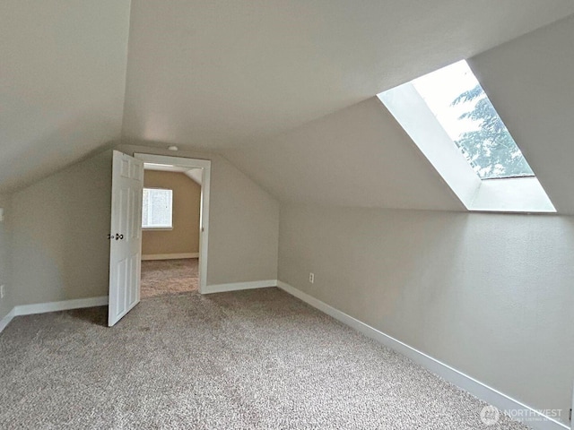 bonus room with lofted ceiling with skylight, carpet flooring, and baseboards