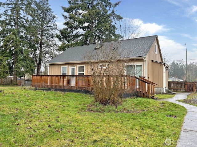 rear view of property with fence, a deck, a lawn, and roof with shingles