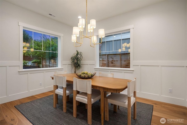 dining room featuring a wainscoted wall, light wood finished floors, visible vents, and a decorative wall