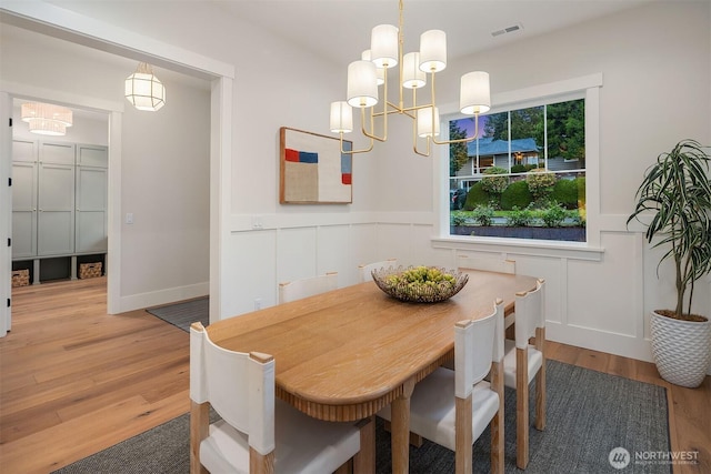 dining area with visible vents, a decorative wall, an inviting chandelier, wainscoting, and wood finished floors