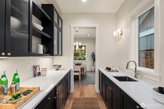 kitchen featuring dark cabinets, a sink, light countertops, open shelves, and decorative light fixtures