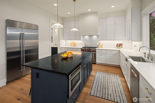 kitchen featuring a center island, white cabinetry, a sink, wall chimney range hood, and built in appliances