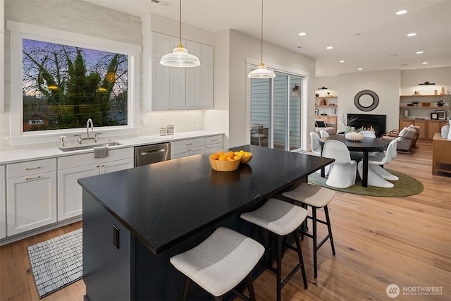 kitchen with light countertops, hanging light fixtures, stainless steel dishwasher, open floor plan, and a sink