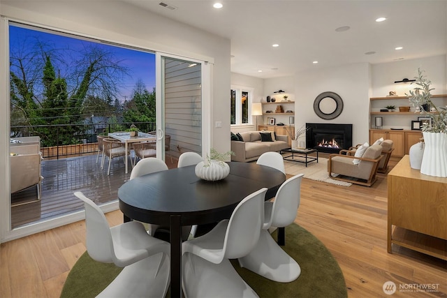 dining room with light wood-type flooring, a glass covered fireplace, visible vents, and recessed lighting