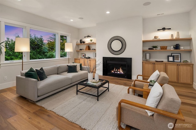 living area featuring a glass covered fireplace, light wood finished floors, and recessed lighting