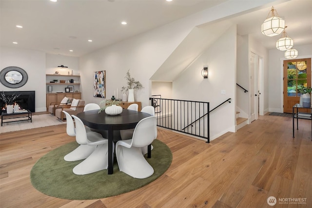 dining space featuring light wood-style floors, a lit fireplace, baseboards, and recessed lighting