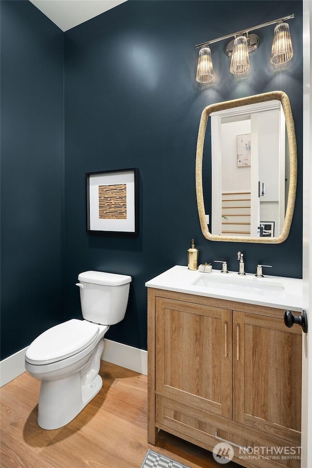 half bath with baseboards, vanity, toilet, and wood finished floors