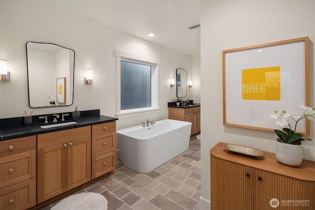 bathroom with a freestanding tub, two vanities, a sink, and recessed lighting