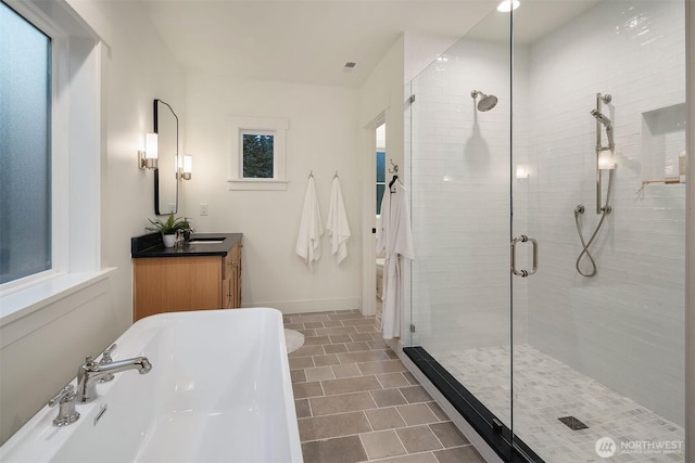 bathroom featuring visible vents, baseboards, vanity, a freestanding tub, and a shower stall