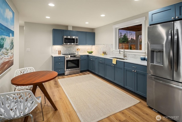 kitchen with blue cabinetry, light countertops, backsplash, appliances with stainless steel finishes, and a sink