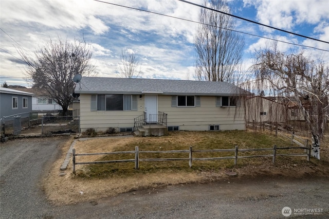 ranch-style home featuring a fenced front yard, roof with shingles, and driveway