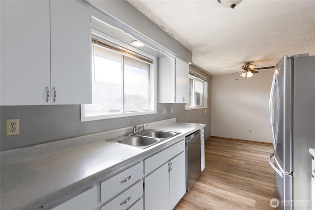 kitchen with light countertops, appliances with stainless steel finishes, white cabinetry, a sink, and light wood-type flooring