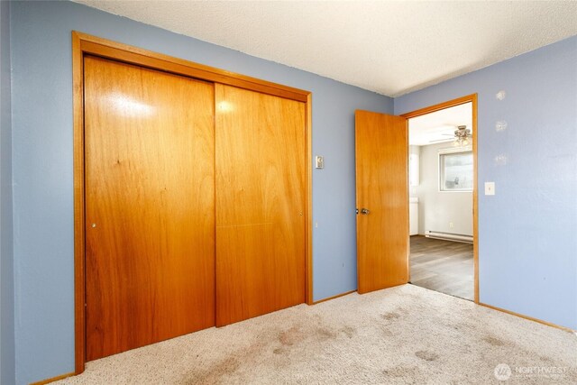 unfurnished bedroom featuring light carpet, a closet, a baseboard radiator, and a textured ceiling