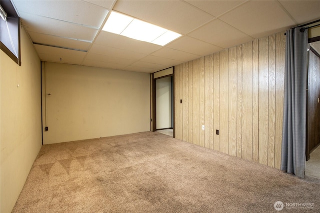 spare room with carpet floors, wood walls, and a drop ceiling