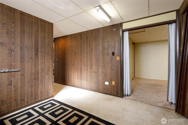 interior space featuring a paneled ceiling, wood walls, and light carpet