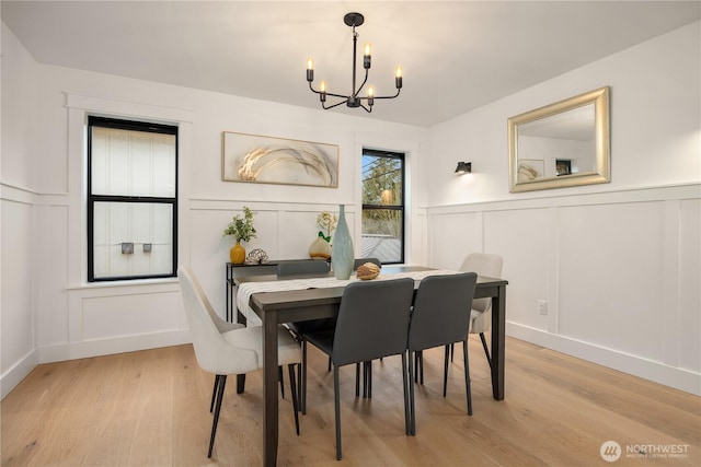 dining area featuring light wood-type flooring, an inviting chandelier, and a decorative wall