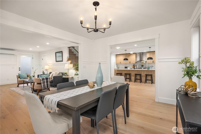 dining room featuring light wood-style flooring, a decorative wall, a notable chandelier, and a wall mounted AC