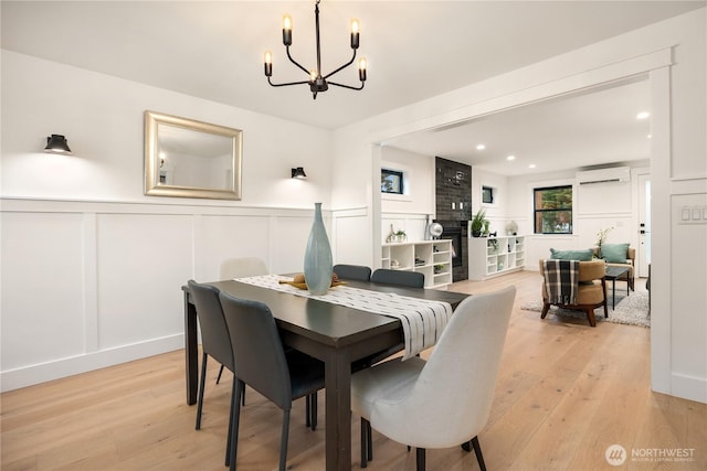 dining space with light wood-style floors, a decorative wall, a wall unit AC, and a notable chandelier