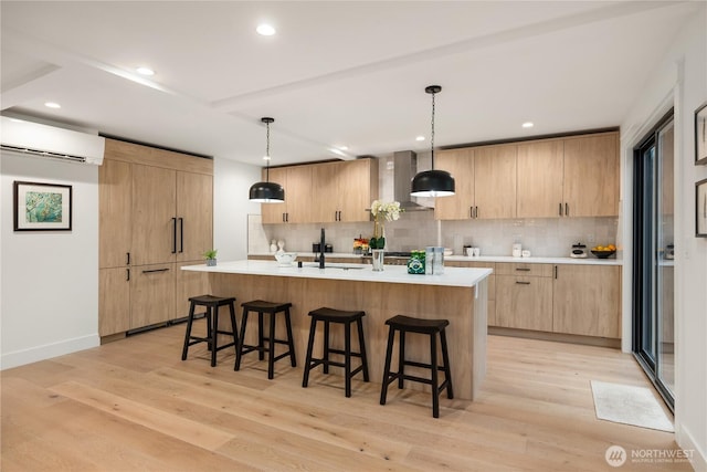 kitchen with a kitchen island with sink, light countertops, hanging light fixtures, and an AC wall unit