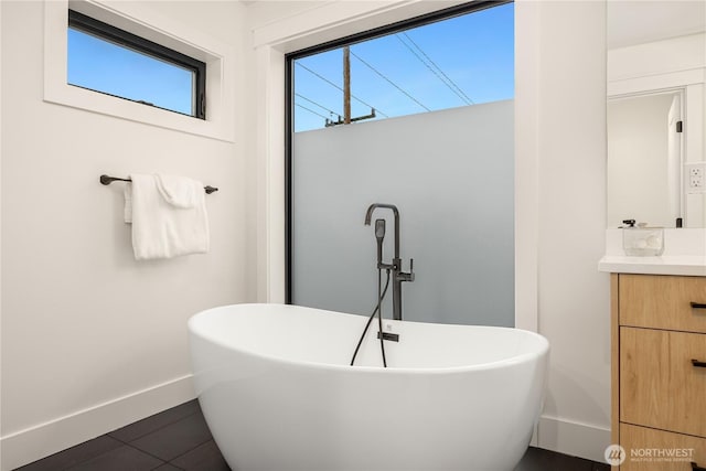 bathroom with a soaking tub, tile patterned flooring, baseboards, and vanity