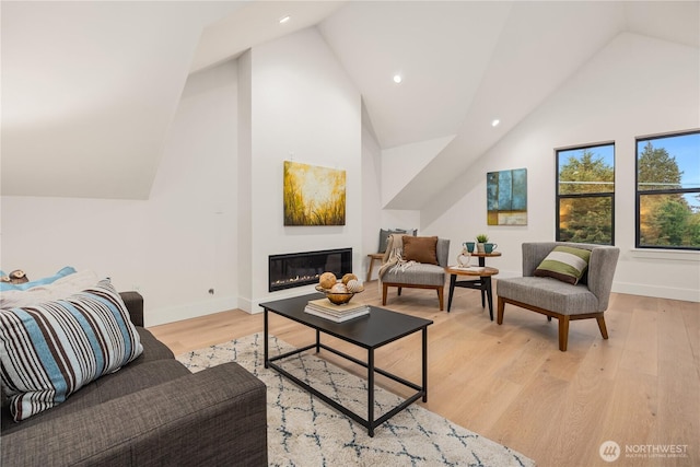 living room featuring light wood finished floors, baseboards, high vaulted ceiling, and a glass covered fireplace