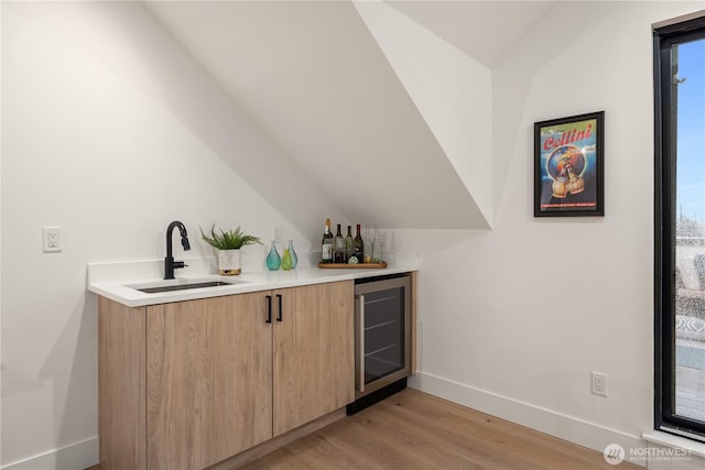 bar featuring beverage cooler, a sink, vaulted ceiling, wet bar, and light wood finished floors