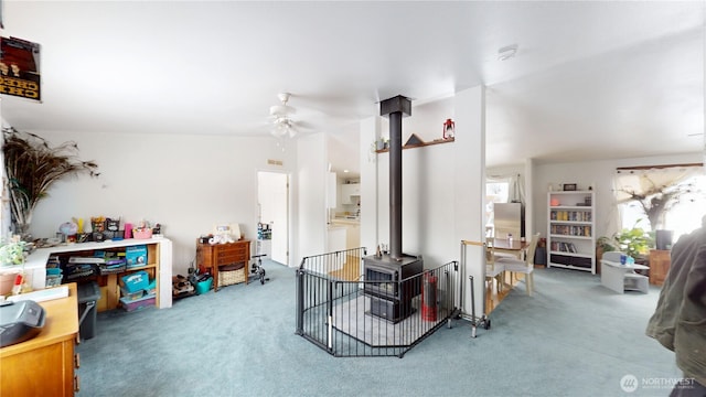 interior space with a ceiling fan, lofted ceiling, a wood stove, and carpet flooring