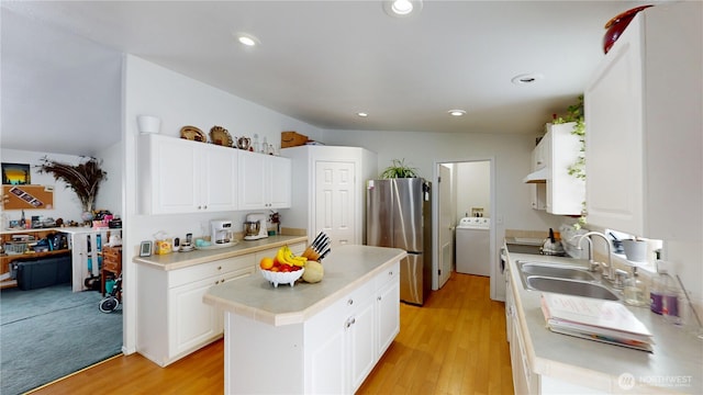 kitchen featuring a kitchen island, washer / clothes dryer, freestanding refrigerator, light countertops, and a sink