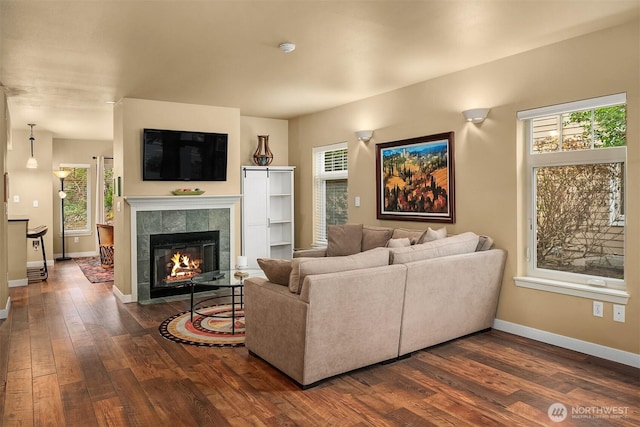 living area with baseboards, dark wood-style flooring, and a tiled fireplace