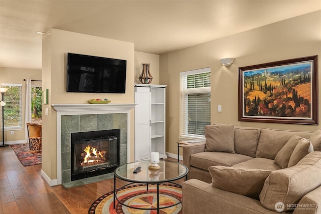 living room with a wealth of natural light, baseboards, wood finished floors, and a tiled fireplace