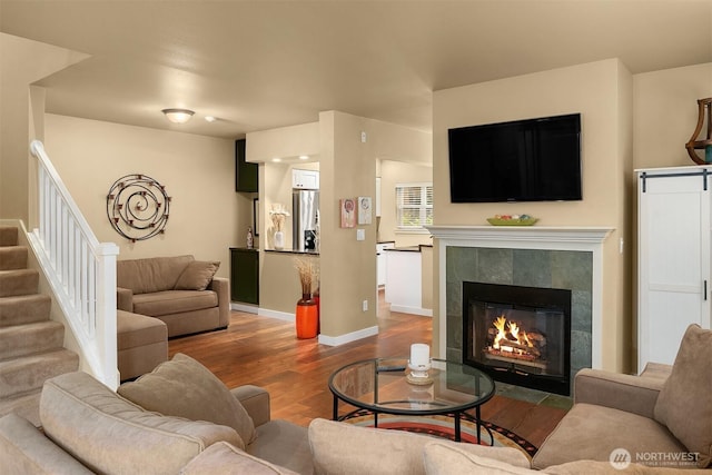 living area with a tiled fireplace, stairway, baseboards, and wood finished floors