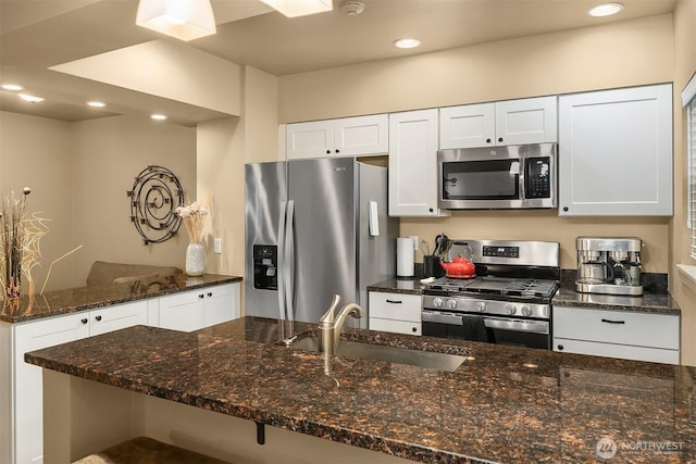 kitchen featuring dark stone countertops, recessed lighting, a sink, appliances with stainless steel finishes, and white cabinetry