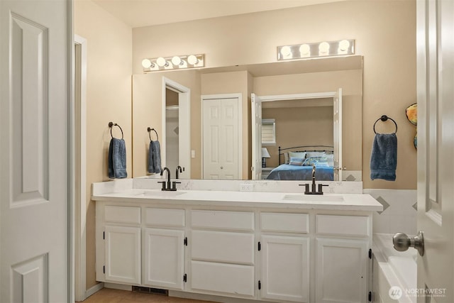 ensuite bathroom with double vanity, connected bathroom, visible vents, and a sink