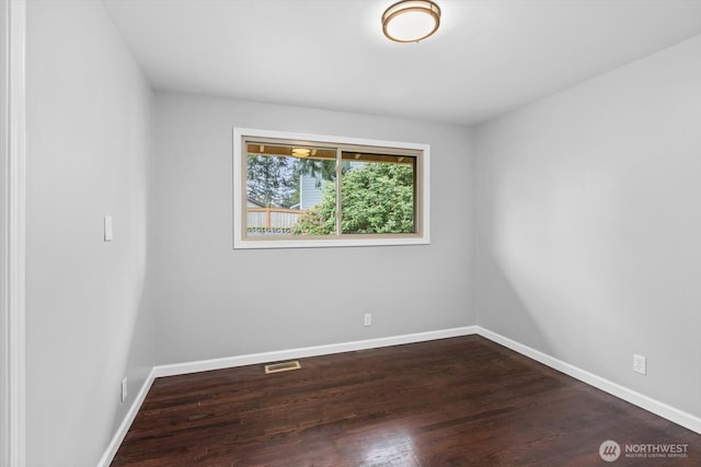 spare room with dark wood-style floors, visible vents, and baseboards