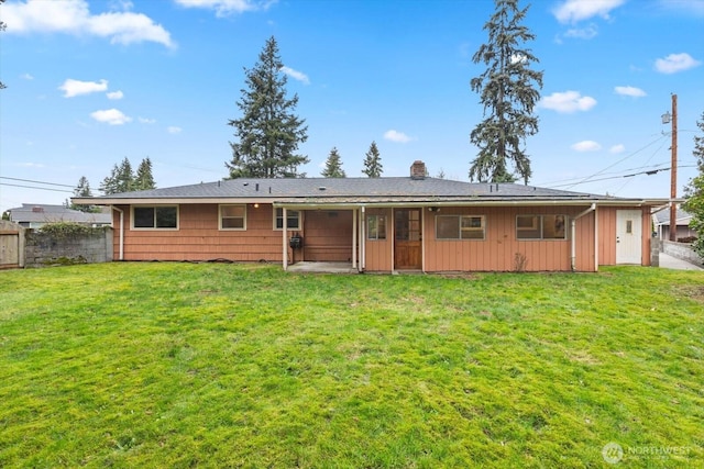 rear view of house with a lawn, a chimney, and fence