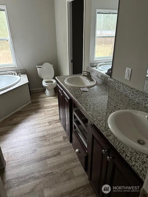 full bath with double vanity, wood finished floors, a sink, and toilet